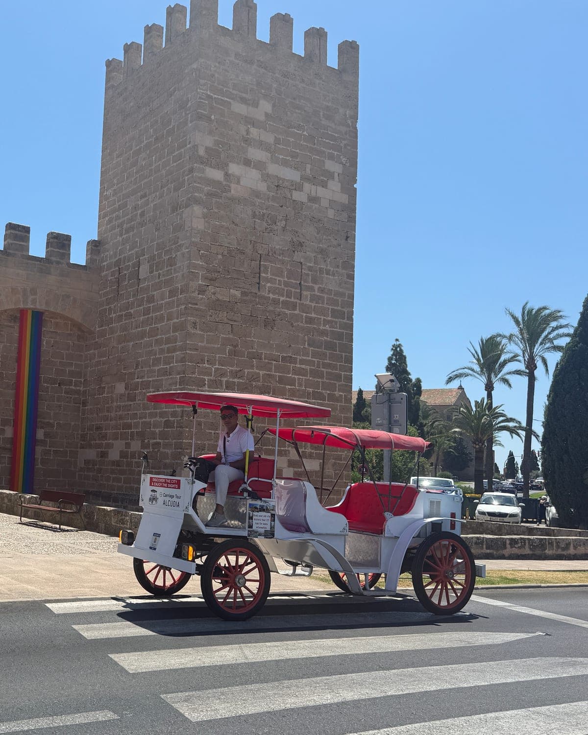 El carruaje eléctrico, rojo y blanco, delante de la Porta de Mallorca, en las murallas de Alcúdia
